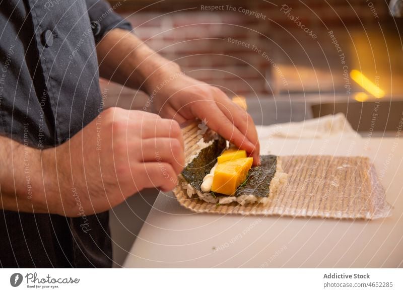 Unbekannter Mann rollt Sushi mit Bambusmatte Küchenchef Rettich rollen Japanisch Asiatische Küche uramaki Unterlage geschmackvoll frisch kulinarisch Restaurant