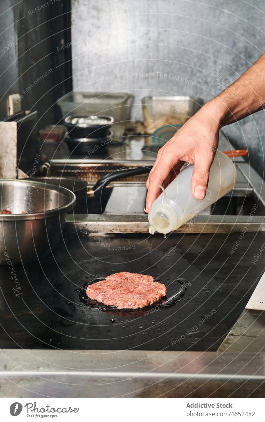 Crop-Koch gießt Öl beim Braten von Burger-Kotelett Küchenchef Pastetchen Fastfood Saucen Junk Food Herd eingießen Flasche Imbisswagen Lebensmittel Arbeit