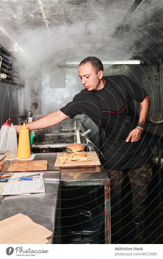 Ein Mann arbeitet in einer Fastfood-Küche Koch Küchenchef Burger Arbeit Junk Food Flasche vorbereiten Saucen Herd männlich Lebensmittel ethnisch kulinarisch Job
