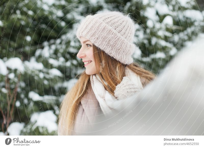 Schöne kaukasische Frau mit langen Haaren zu Fuß im Winter Wald mit Schnee auf ihre gestrickte Mütze. Wintermode und stilvolles Outfit. Echte Menschen, die Spaß im Winter, genießen die frische Luft in der Natur mit verschneiten Tannen.
