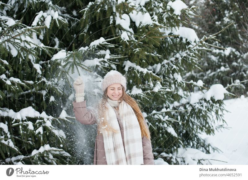 Schöne kaukasische Frau mit langen Haaren zu Fuß im Winter Wald mit Schnee auf ihre gestrickte Mütze. Wintermode und stilvolles Outfit. Echte Menschen, die Spaß im Winter, genießen die frische Luft in der Natur mit verschneiten Tannen.