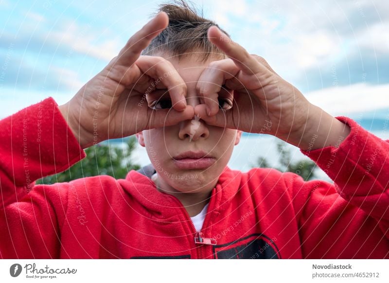 Porträt eines 9-jährigen Jungen im Freien, mit den Händen um die Augen, als ob er ein Fernglas benutzen würde, in Freizeitkleidung 9 Jahre alt gestikulieren