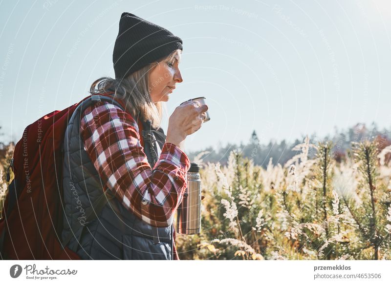 Frau macht Pause und entspannt sich mit einer Tasse Kaffee während eines Sommerausflugs. Frau steht auf dem Weg und schaut weg. Frau mit Rucksack Wandern durch hohes Gras entlang Weg in den Bergen