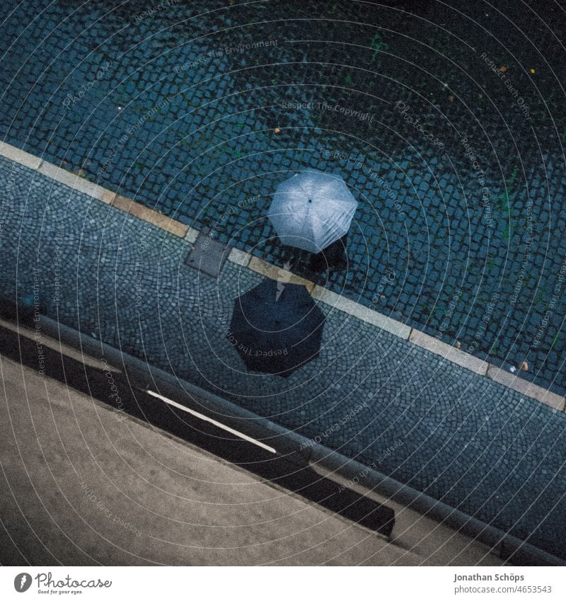 Vogelperspektive auf zwei Personen mit Regenschirm auf Straße bei Regen nass Pflastersteine gepflastert Fußweg schlechtes Wetter Regenschutz grafisch