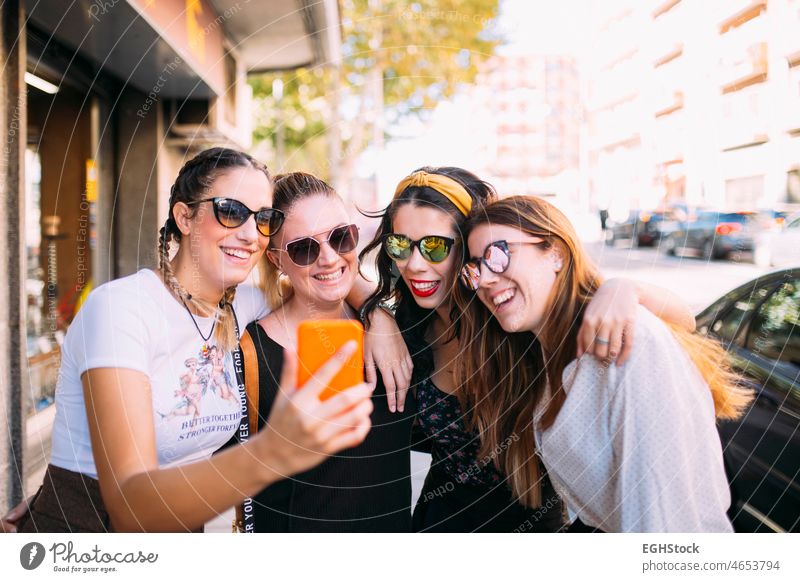 Gruppe von 4 jungen Freundinnen, die einen sonnigen Tag in der Stadt genießen und für ein Foto posieren und geradeaus schauen sorgenfrei heiter Großstadt