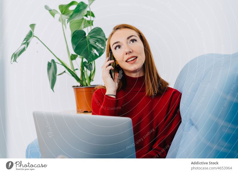 Junge Frau mit Laptop im Gespräch am Telefon Telefonanruf Smartphone benutzend reden Kommunizieren Anschluss online Arbeit ruhen zu Hause sprechen Netbook Liege