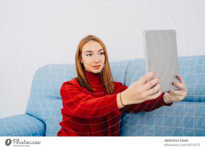Frau auf Sofa nimmt Selfie auf Tablet Selbstportrait Tablette benutzend Liege räkeln Kälte Komfort ruhen Rotschopf fotografieren Gedächtnis schießen sitzen