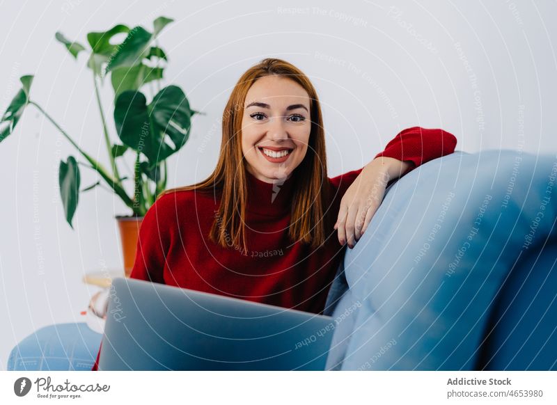 Fröhliche Frau mit Laptop auf der Couch zu Hause benutzend freiberuflich online Internet Freizeit abgelegen Arbeit Glück Browsen Tippen Surfen Netbook
