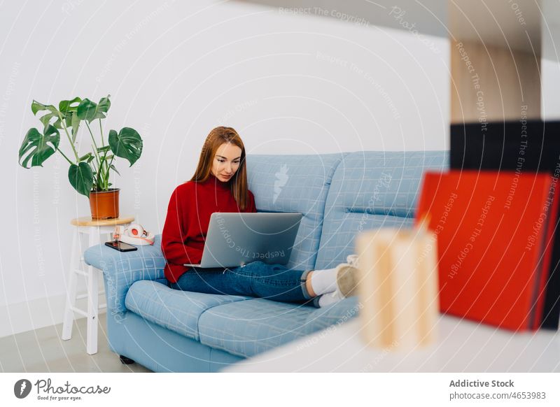 Fröhliche Frau mit Laptop auf der Couch zu Hause benutzend freiberuflich online Internet Freizeit abgelegen Arbeit Glück Browsen Tippen Surfen Netbook