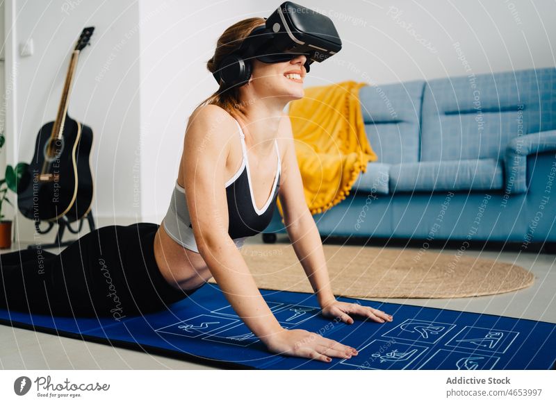 Lächelnde Frau mit VR-Brille übt Yoga üben benutzend Virtuelle Realität Schutzbrille Kobra-Pose bhujangasana Asana Sportbekleidung Headset online Unterlage