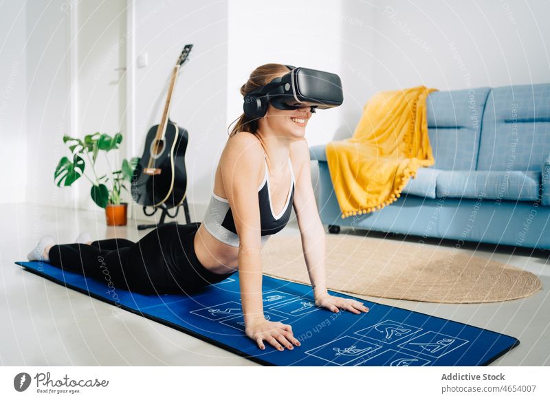 Lächelnde Frau mit VR-Brille übt Yoga üben benutzend Virtuelle Realität Schutzbrille Kobra-Pose bhujangasana Asana Sportbekleidung Headset online Unterlage