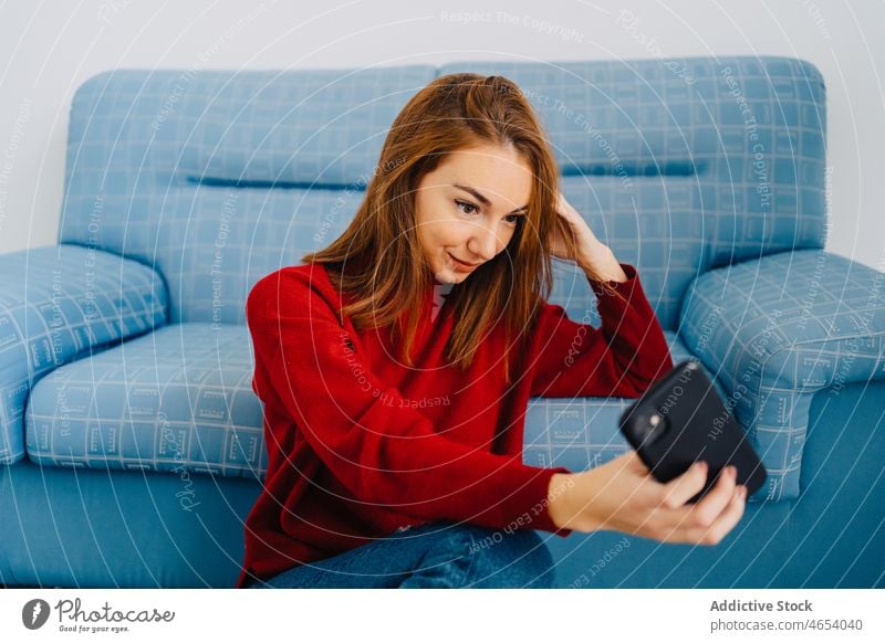 Frau auf dem Sofa macht Selfie mit Smartphone Selbstportrait benutzend Liege räkeln Kälte Komfort ruhen Rotschopf fotografieren Gedächtnis schießen Gerät sitzen