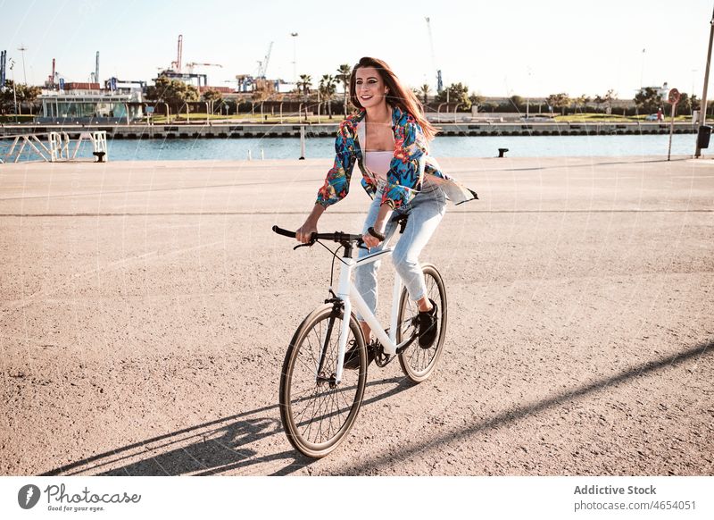Lächelnde Frau auf dem Fahrrad an einer Böschung Fluss Großstadt Park Aktivität Sommer Wochenende Stauanlage Hobby Mitfahrgelegenheit Freizeit heiter sorgenfrei