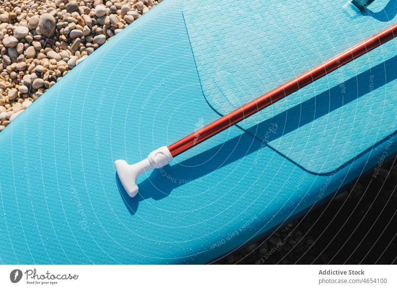 Blaues SUP-Board und Paddel zum Surfen an steinigen Ufern Paddelbrett Brandung Surfbrett Zusatzplatine MEER Aktivität Wasser Gerät Sonne Meeresufer Kieselsteine