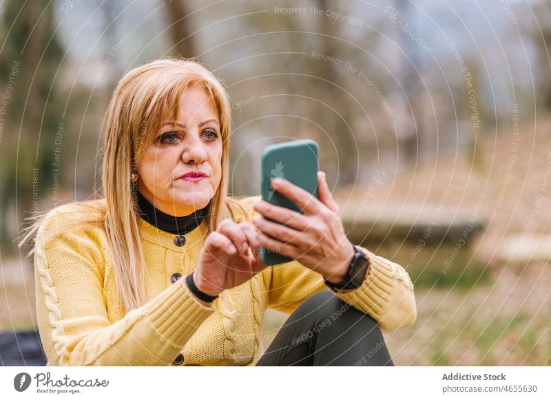 Ältere Frau, die im Park auf ihrem Smartphone surft Browsen Textnachricht online Internet Talkrunde Lebensmitte Anschluss Vorschein feminin Stil Umwelt