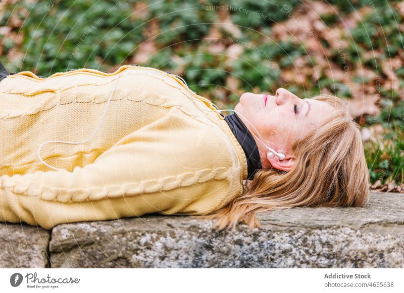 Frau hört Musik, während sie im Park liegt zuhören Kopfhörer meloman Gesang Herbst Wiedergabeliste Melodie Smartphone Funktelefon Lebensmitte Augen geschlossen