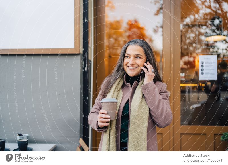 Ethnische Frau mit Tasse Kaffee bei einem Telefonat auf einem Smartphone Smartphone Telefonanruf Lächeln benutzend sprechen Gespräch Imbissbude reden Glück