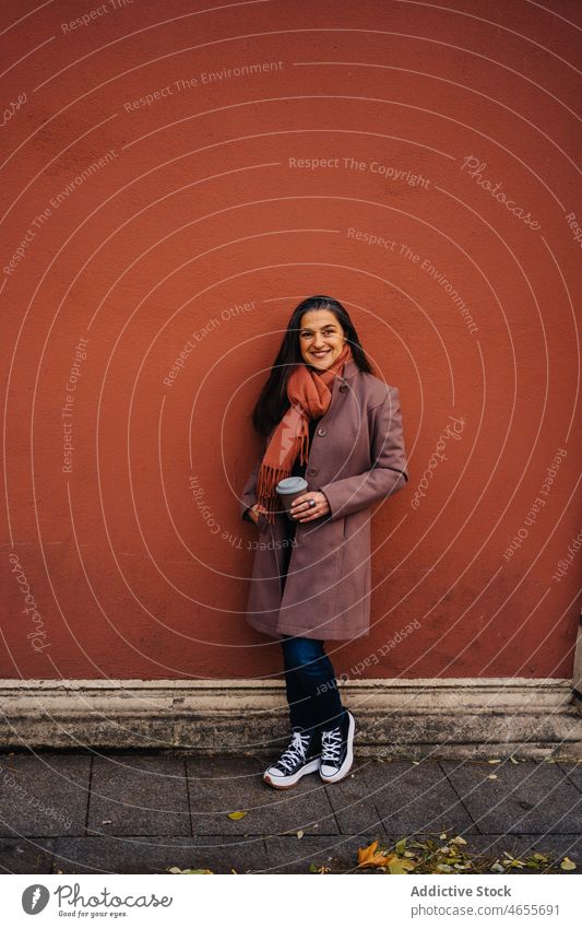 Hispanische Frau mit Kaffeetasse an der Wand Imbissbude Lächeln zum Mitnehmen heiter Getränk Glück Bürgersteig urban Erwachsener reif Straßenbelag stehen