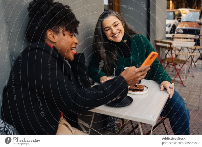 Fröhliche schwarze Frau zeigt Smartphone an ethnischen Freund Frauen teilen zeigen benutzend Sitzung Glück heiter Lächeln zuschauen Freude Funktelefon Surfen