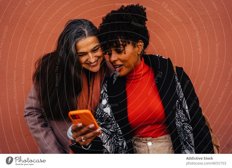 Positiv gestimmte Damen mit Smartphone auf rotem Hintergrund Frauen Freund Funktelefon Zusammensein benutzend Zeit verbringen Texten Telefon Lächeln SMS