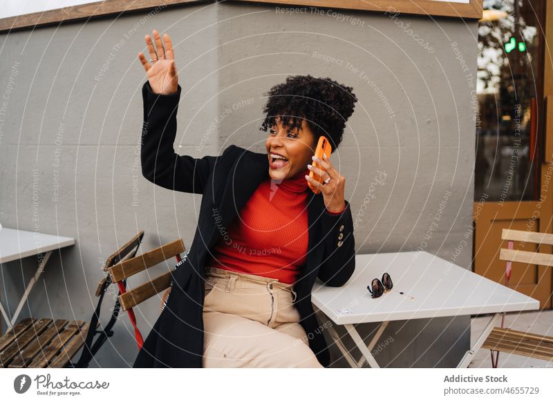 Fröhliche schwarze Frau, die mit ihrem Smartphone spricht und mit der Hand winkt aufgeregt benutzend Telefonanruf Gruß Glück Hallo Wellenhand cool froh