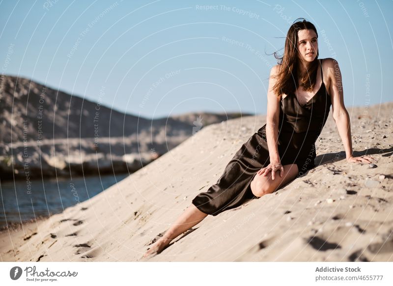 Schlanke attraktive Frau sitzt auf Sandstrand in sonnigen Tag wüst Sommer wolkenlos Meeresufer Blauer Himmel Barfuß Seeküste Sonne Kleid Harmonie Sonnenkleid