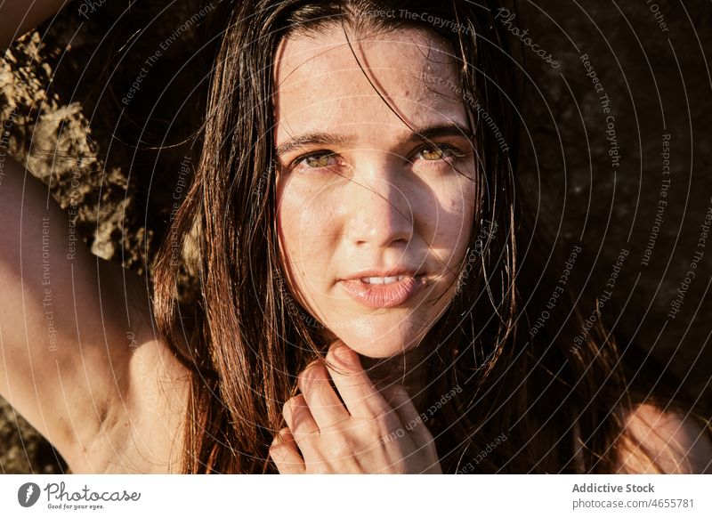 Junge Frau mit nassen Haaren lehnt sich an eine Felsformation felsig Felsen Klippe lange Haare Sonnenlicht attraktiv charmant Windstille Porträt Vorschein Natur