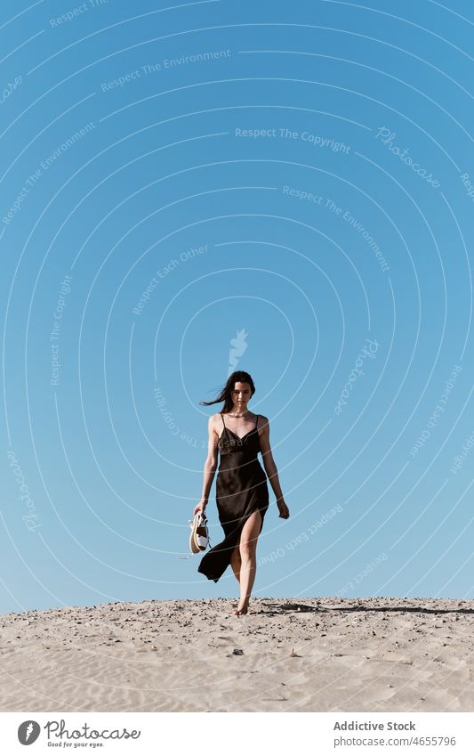 Schlanke attraktive Frau, die an einem sonnigen Tag am Sandstrand spazieren geht wüst Sommer wolkenlos Blauer Himmel Barfuß Sonne Kleid Harmonie Sonnenkleid