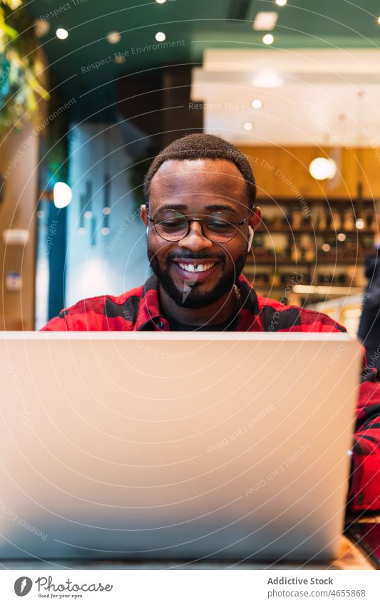 Lächelnder schwarzer Mann arbeitet an einem Laptop in einem Café Kopfhörer benutzend online Internet Browsen freiberuflich Arbeit männlich Afroamerikaner