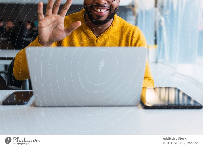 Lächelnder schwarzer Mann, der am Laptop im Arbeitsbereich telefoniert Videoanruf Kopfhörer benutzend Video-Chat online Kommunizieren Büro männlich