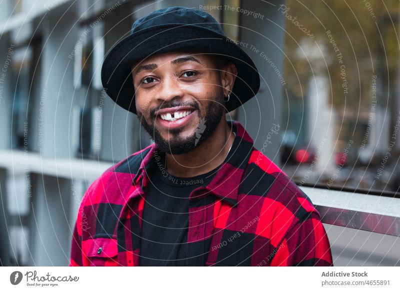 Fröhlicher schwarzer Mann in stilvollem Outfit auf der Straße Stil Großstadt Vorschein Individualität Persönlichkeit kariertes Hemd Hut männlich Afroamerikaner