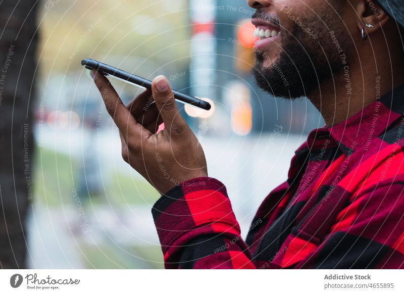 Anonymer schwarzer Mann spricht auf der Straße mit seinem Smartphone Sprachmeldung benutzend Großstadt Kommunizieren Audio online Internet urban männlich