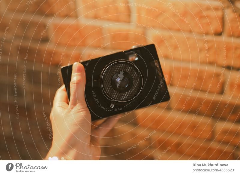 Hand hält Retro Vintage-Kamera in einem Raum mit gemütlichen Beleuchtung und roten Backsteinmauer. Retro Vintage Fotoapparat in der Hand horizontales Foto.