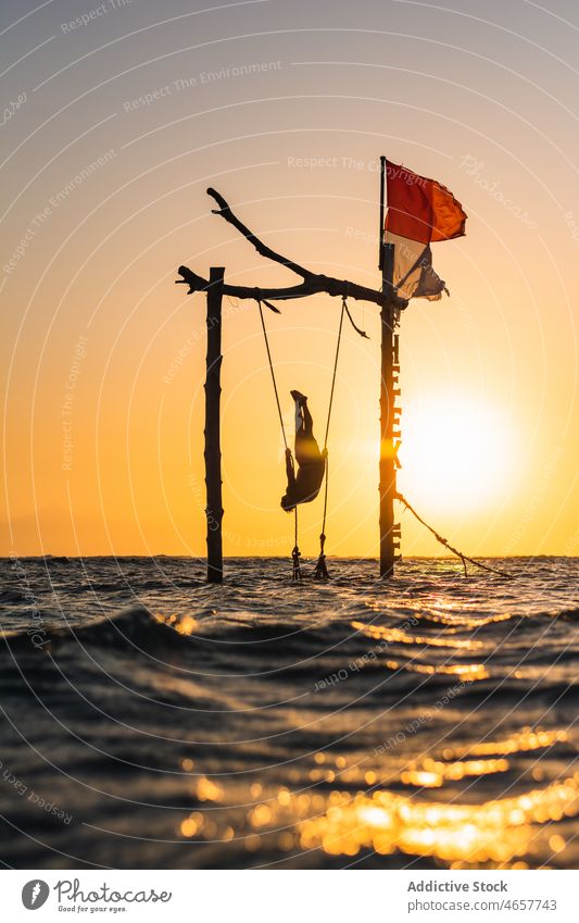 Silhouette einer Person, die an einer Schaukel im Meer hängt Tourist hängen pendeln MEER tropisch exotisch Sonnenuntergang Urlaub Natur auf den Kopf gestellt