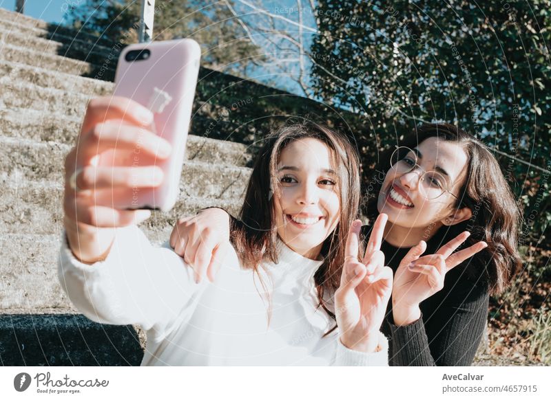 Zwei junge Studenten sitzen im Freien machen Selfie mit dem Telefon, Universitätsgebäude auf dem Hintergrund und Blick auf Smartphone. Junge Frau feiert Studie auf trendige Kleidung super Lächeln, Multi-Rassen