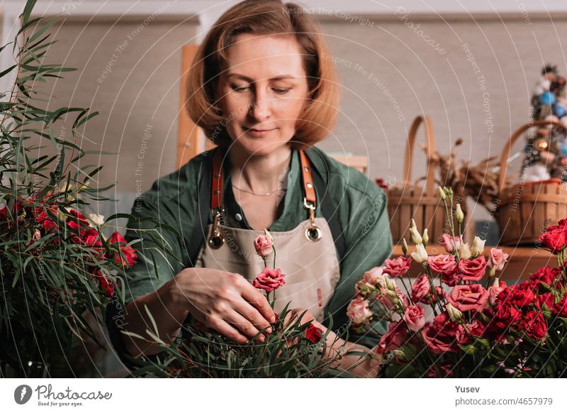 Schöne Frau Florist macht ein Geschenk Strauß Rosen. Florist Arbeitsplatz. Kleines Geschäftskonzept. Frontansicht. Blumen und Zubehör. Selektiver Fokus schön