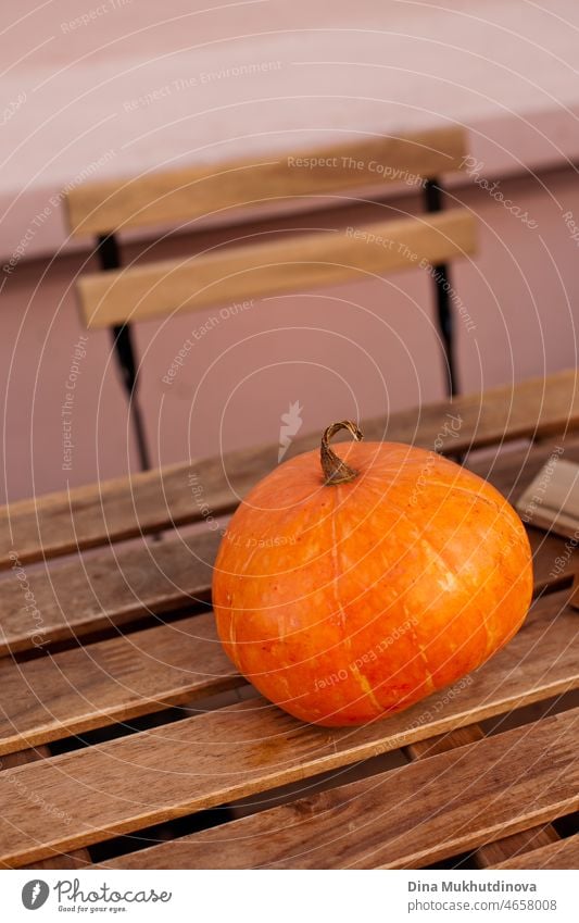 Ein reifer orangefarbener Kürbis auf einem Holztisch auf der Terrasse zu Hause oder im Innenhof eines Restaurants. Kleine Größe Kürbis auf alten Holztisch.