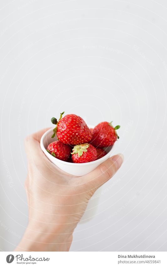 Hand hält einen weißen Pappbecher mit frischen reifen Erdbeeren auf weißem Hintergrund. Erdbeeren im Becher und Kopierraum oben. Textfreiraum Frühstück roh