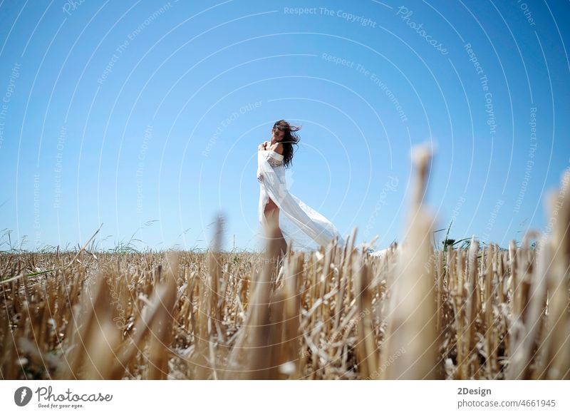 Eine einsame Frau mit langen, gewellten Haaren und einem weißen Kleid genießt ein Weizenfeld bei Sonnenuntergang. Landschaft Sommer Lifestyle Schönheit Freiheit