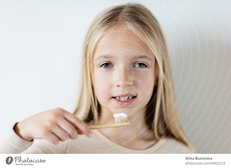 Nettes kleines Mädchen hält Hände Öko-Bambus-Zahnbürste auf beige Hintergrund. Nachhaltiges Lebenskonzept. Speichern Sie den Planeten für unsere Kinder