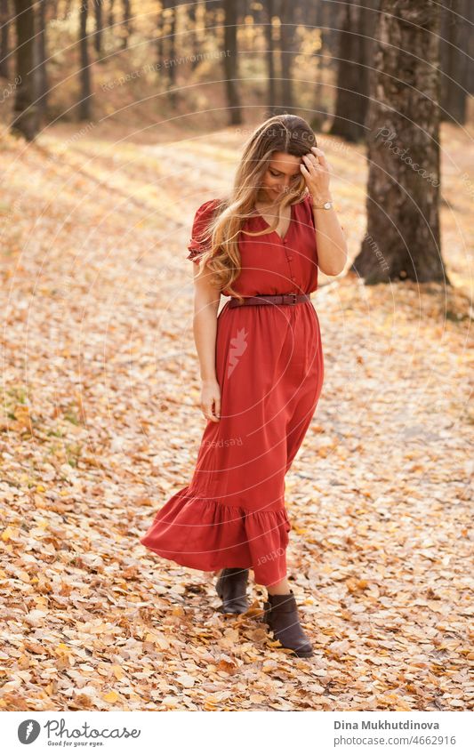 schöne Frau mit langen in rotem Kleid zu Fuß in den Wald zwischen Bäumen. Romantischer Spaziergang im Wald im Herbst Natur auf Herbstblätter. Erwachsener