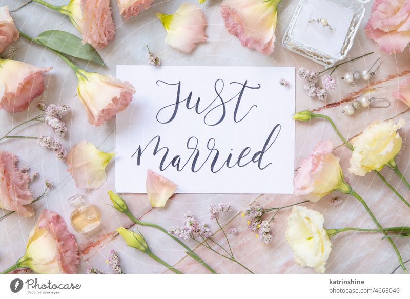 Karte mit dem Text JUST MARRIED umgeben von rosa Blumen Einfach verheiratet Hochzeit Postkarte handschriftlich Draufsicht Murmel Tisch Papier zitieren Heirat