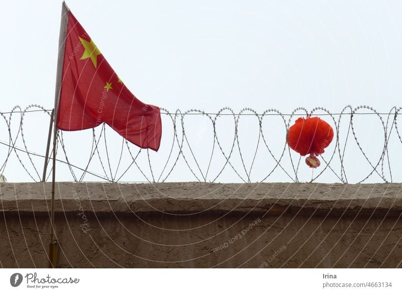 Chinesische Flagge vor Stacheldraht mit rotem Lampion China chinesische flagge regime Xinjiang eingesperrt bedrohlich bedrückt Misstrauen Wachsamkeit Hausmauer