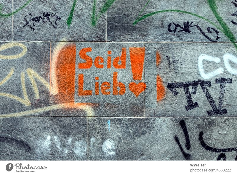 An einer bekritzelten Wand steht in oranger Farbe die Aufforderung "Seid Lieb!" Mauer Graffiti Schrift Zeichen Schriftzeichen Worte rot farbig Bitte Herz
