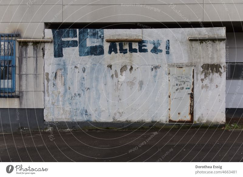 Fassade mit Fenster und Tür an einer alten Halle mit Fußballfan-Graffito Gebäude verlassen vernachlässigt trist blau Schrift von außen Wand weiß fleckig