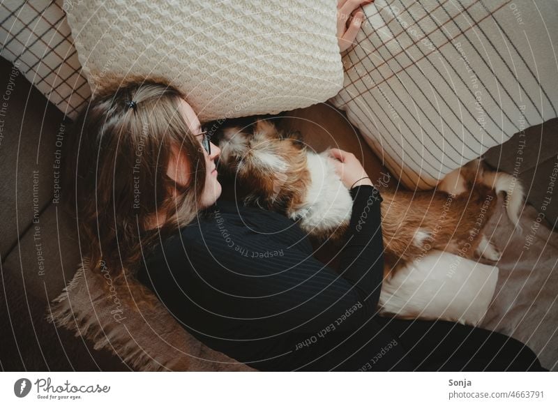 Eine junge Frau liegt mit einem kleinen Hund auf einer Couch. Lifestyle Glück Freundschaft Tier Haustier Zusammensein zuhause Liebe Zusammengehörigkeitsgefühl