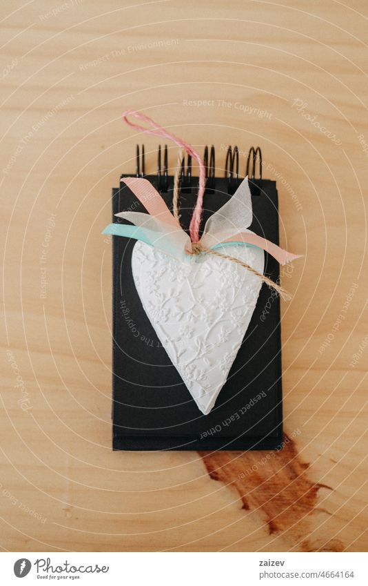 Notebook mit schwarzen Laken auf einem Holztisch mit einem weißen Herz. Buch Papier Tisch Attrappe nach oben Textfreiraum Hinweis Hintergrund Arbeitsbereich