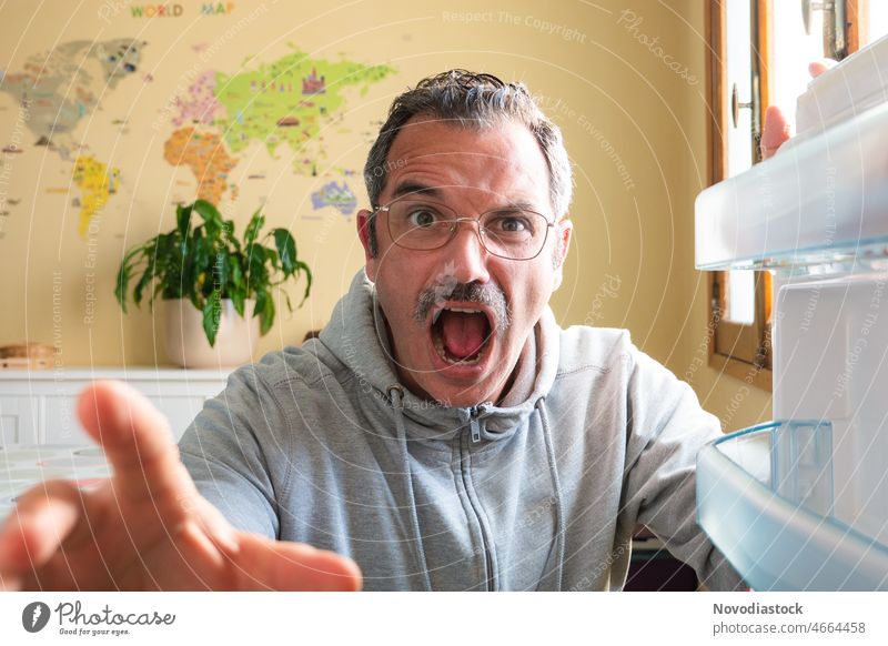 Porträt eines 45-jährigen Mannes mit Brille und Freizeitkleidung an der Kühlschranktür, der schockiert aussieht mittleres Alter Kaukasier Schnurrbart