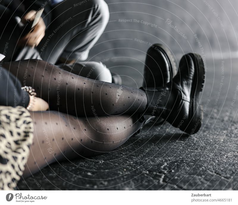 Beine einer Frau mit Netzstrumpfhose und schwarzen Boots, auf Boden sitzend Stiefel ausgestreckt warten Ausstellung cool Schuhe Strumpfhose Bekleidung feminin