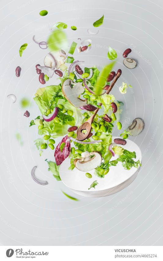 Gesunder grüner Salat fliegt über eine weiße Schüssel. Gesundheit Salatbeilage fliegend Schalen & Schüsseln bei Weiß Pilze Kidney Bohnen Edamame Zwiebel Wand